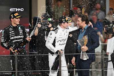 Die Schauspieler Brad Pitt (im weißen Rennanzug) und Javier Bardem auf dem Podium in Abu Dhabi. Links im Bild: Mercedes-Pilot George Russell