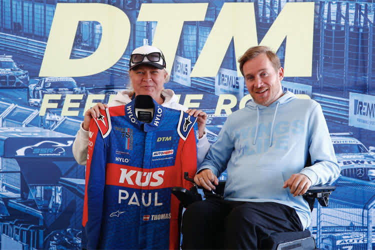 Wings for Life-Botschafter Samuel Koch (r) bei der Übergabe des Rennanzugs von Porsche-Werksfahrer Thomas Preining an die Gewinnerfamilie der letzten DTM-Auktion der Saison