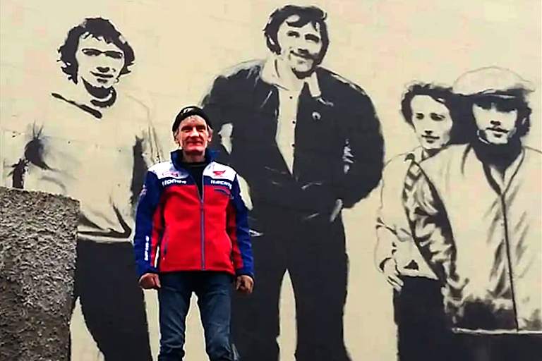 Chris Meyer vor der Hausmauer mit dem Bild der Mitglieder der Armoy Armanda